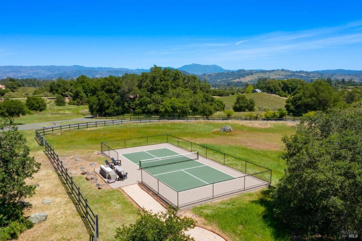 A tennis court is surrounded by a fence and overlooks a rural landscape. 