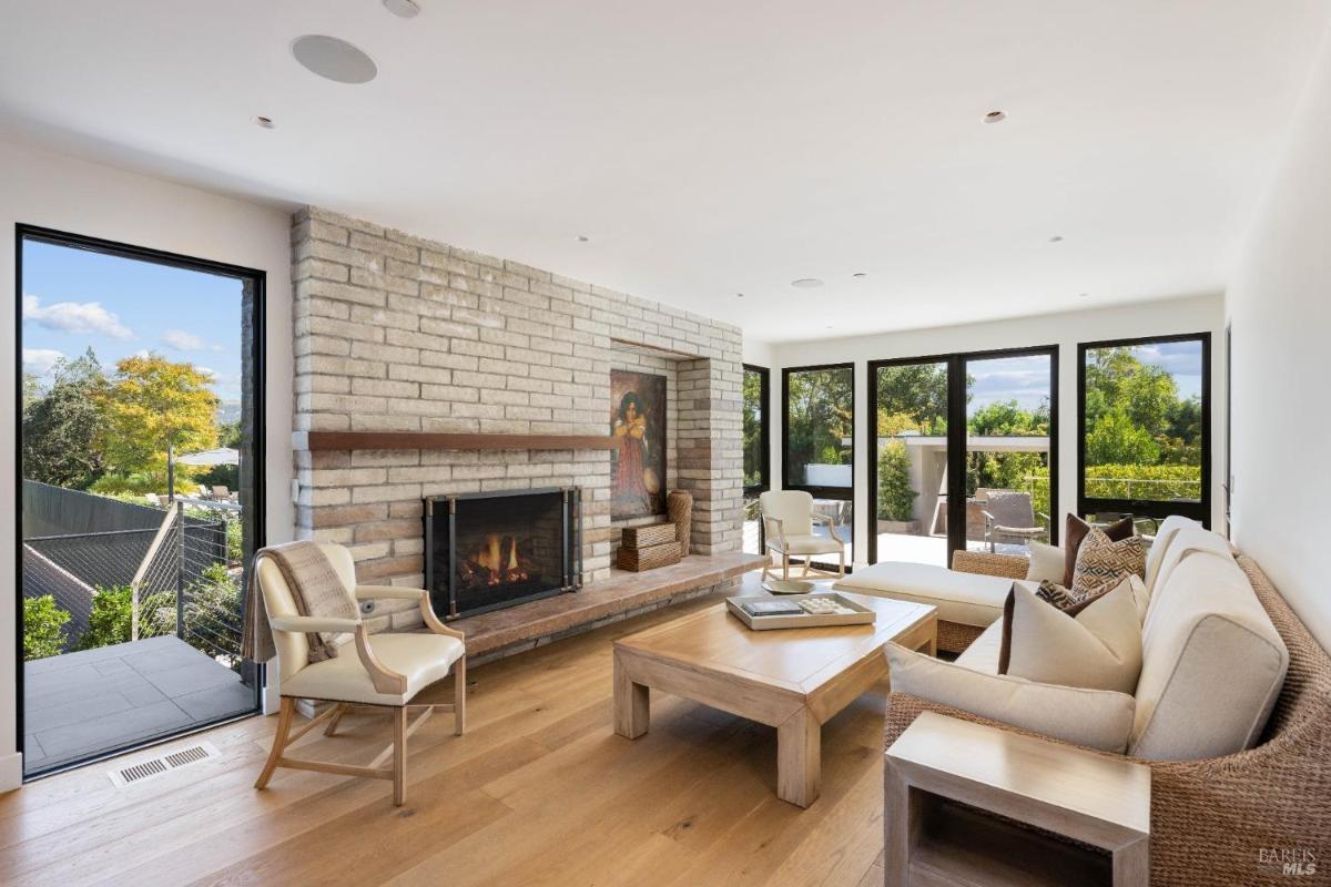 Living space with a brick fireplace, beige seating, a wooden coffee table, and multiple glass doors opening to a garden area.