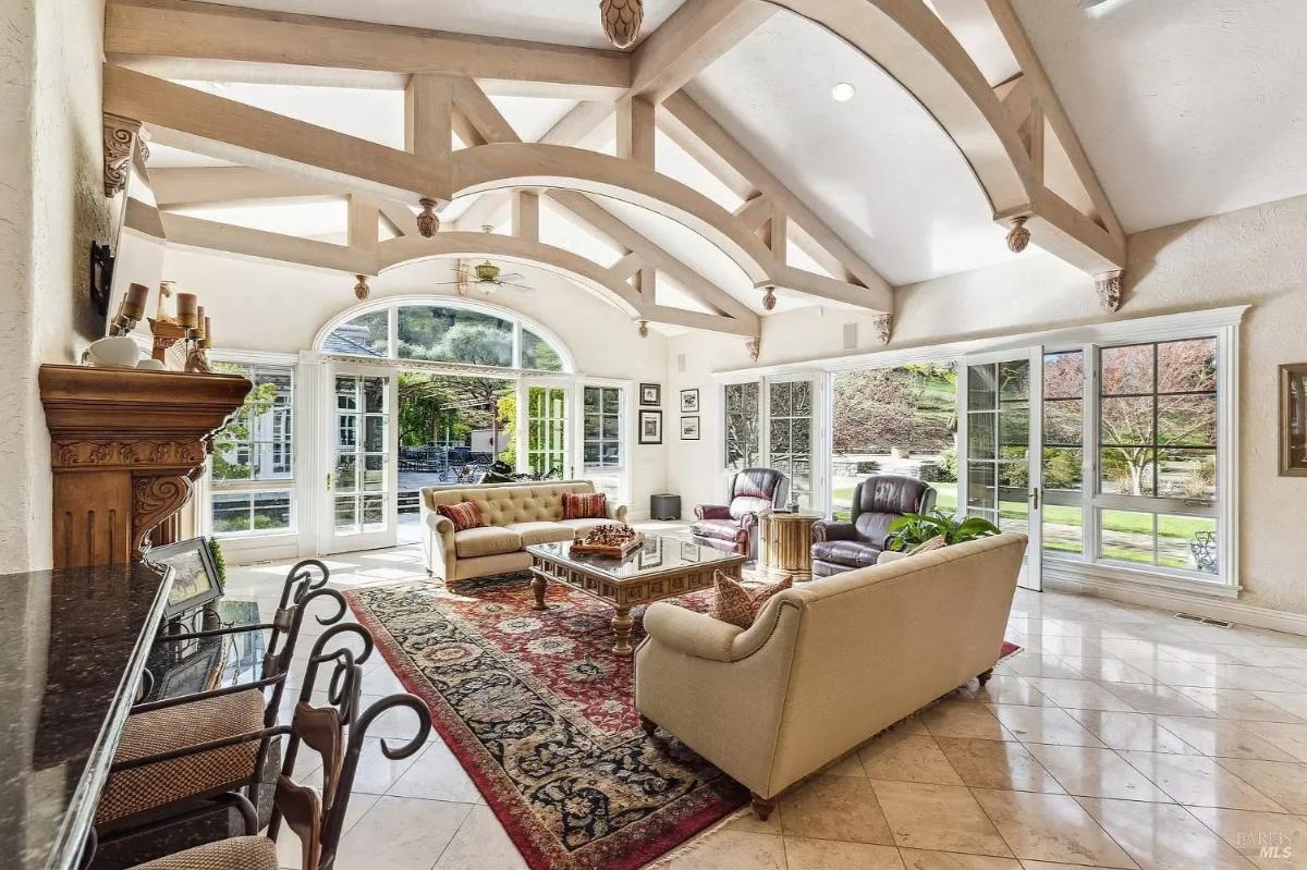 Living area with a rug, sofas, and exposed wooden beams on a high ceiling.