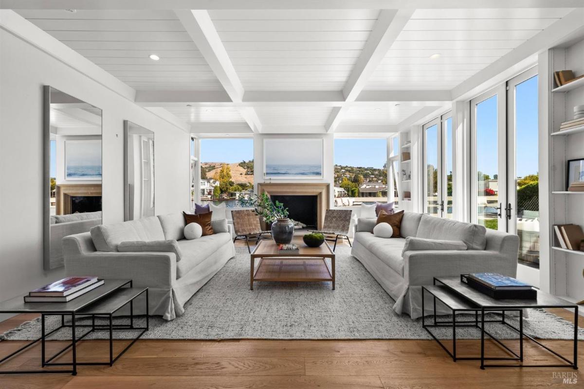 A living room with two white sofas, a coffee table, and large windows with outdoor views.