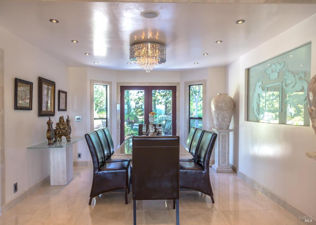 A dining area with a table and six chairs, a chandelier above, and large windows. 