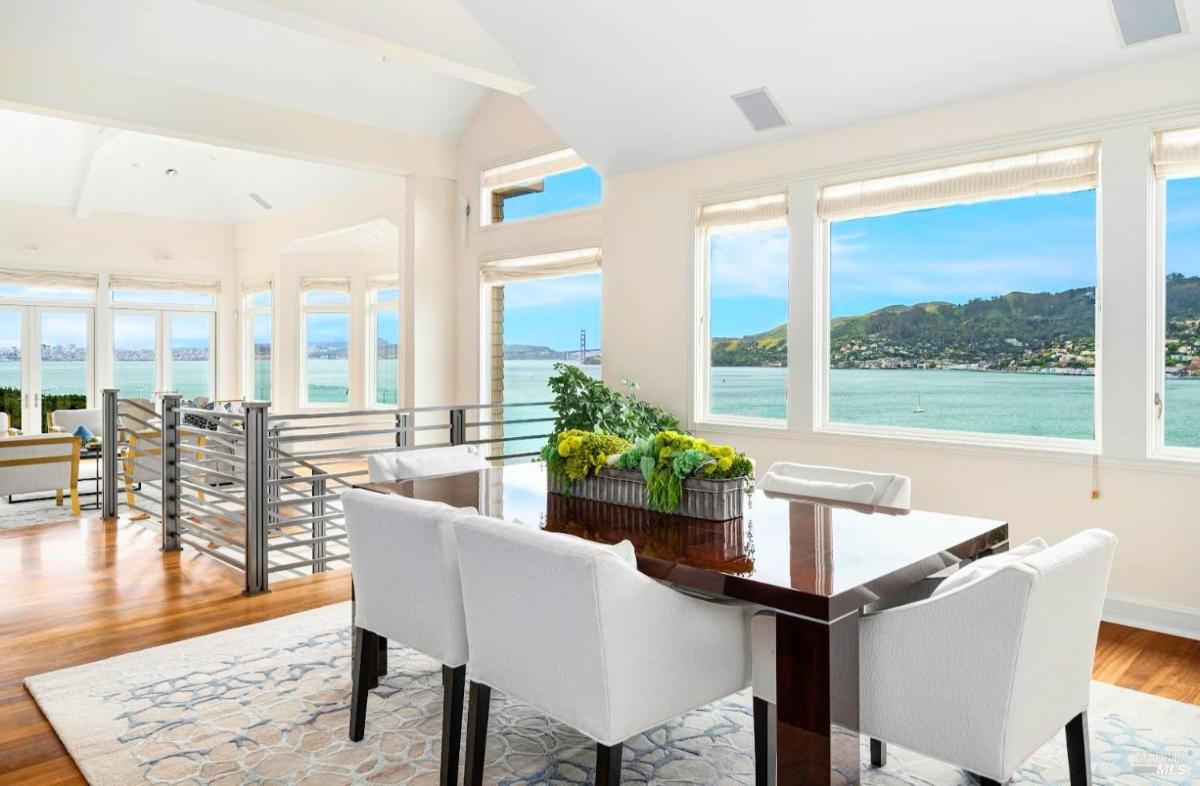 Dining area with table and chairs, featuring large windows with water views.