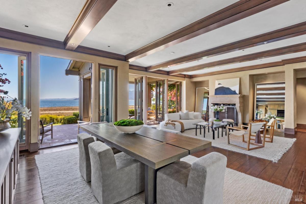 Spacious dining area with dining table, curved sofa, coffee table, chairs, fireplace, and large windows showcasing a scenic view.