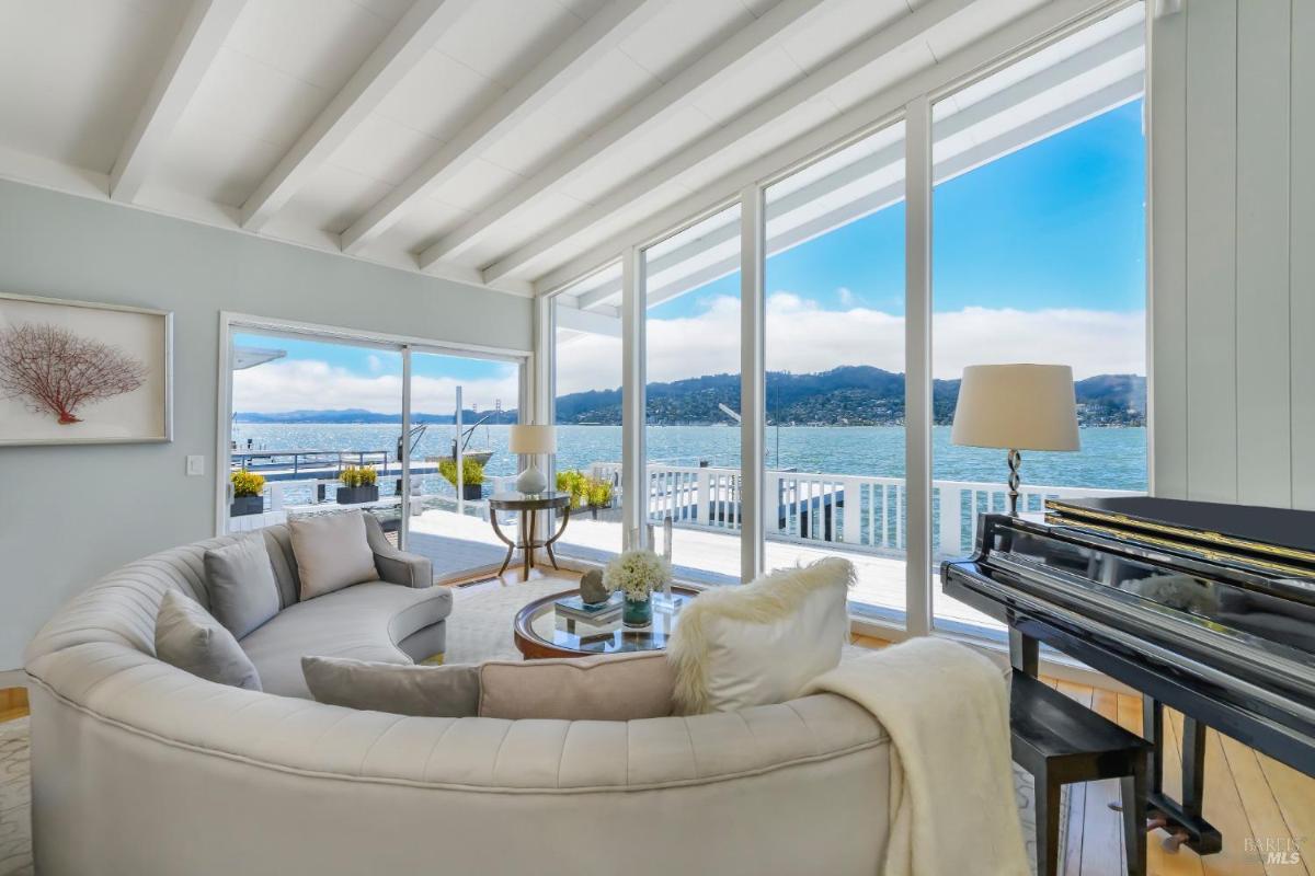 Lounge area with curved couch, piano, and floor-to-ceiling windows overlooking the water.