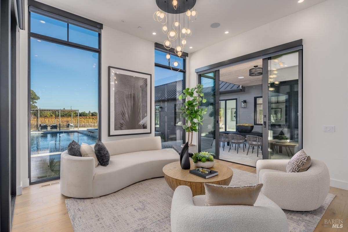 Living room with floor-to-ceiling windows, round coffee table, white seating, and a central light fixture.