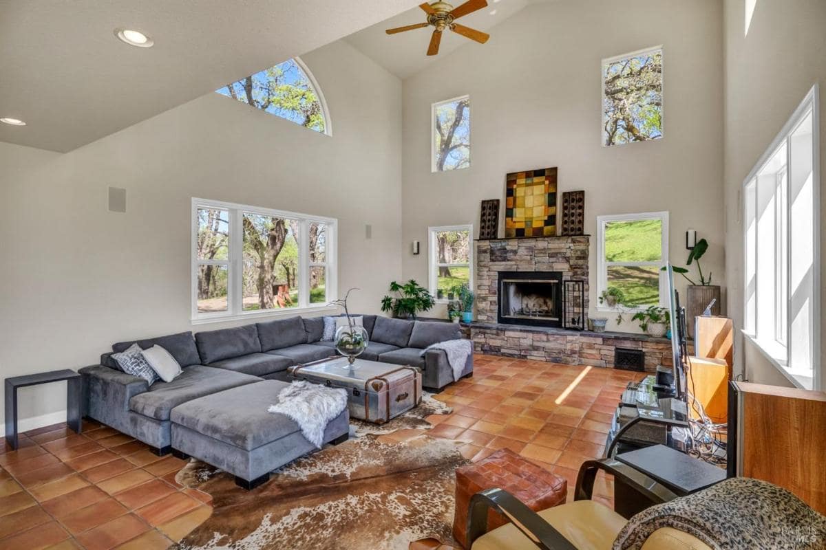 Living room with a large sectional sofa, a stone fireplace, and abundant natural light from the windows. 