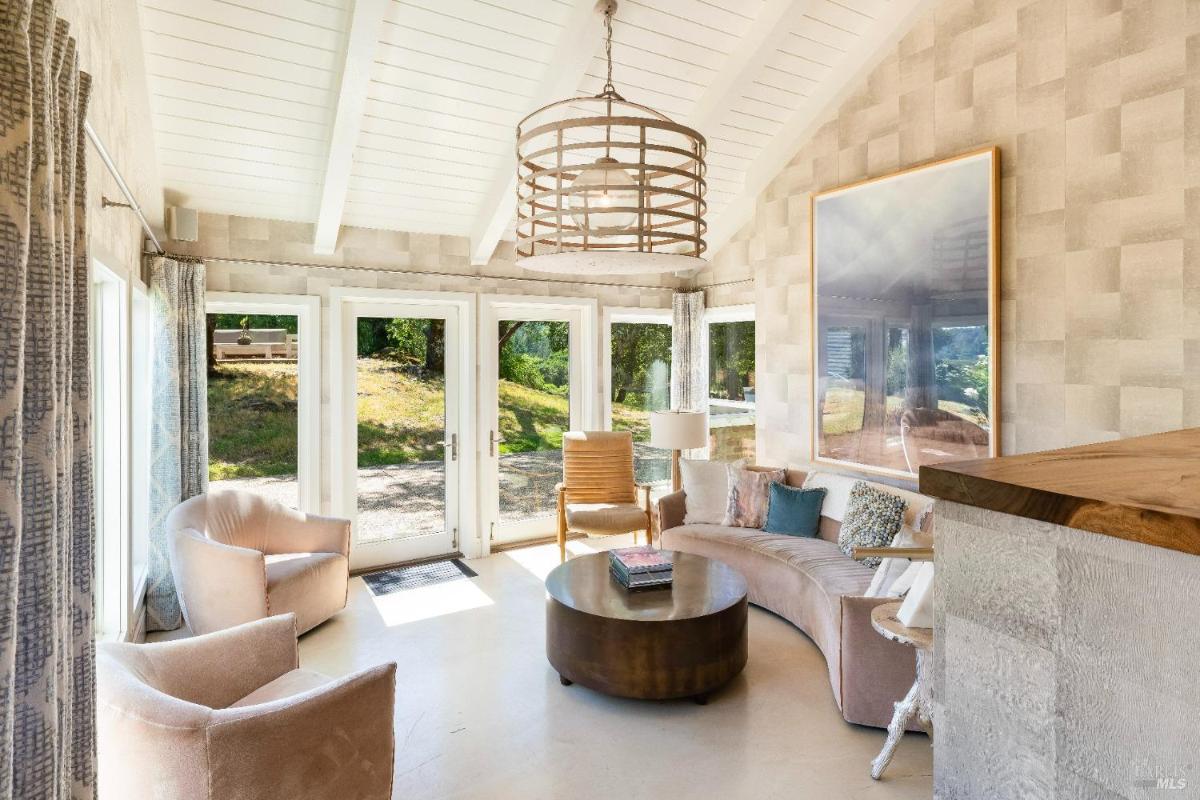 Sunlit living room with large windows, curved sofa, and armchairs.