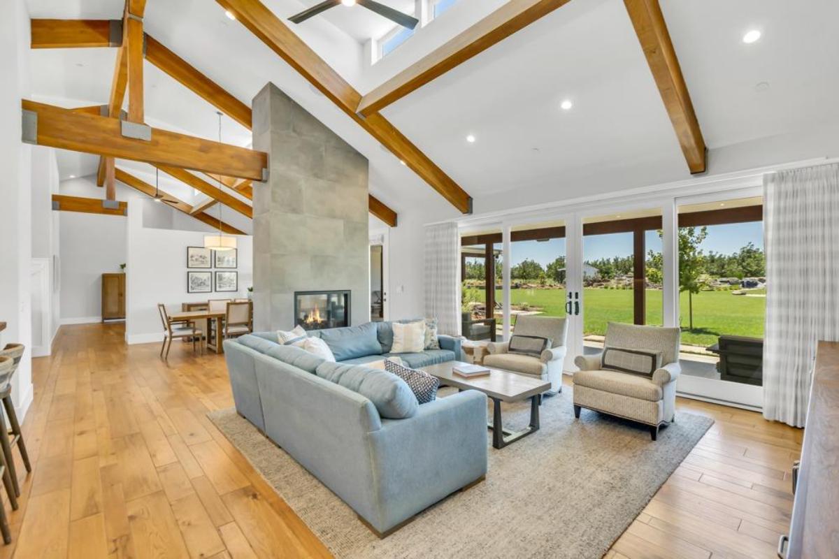 A living room with exposed beams, a central fireplace, and views of the yard.