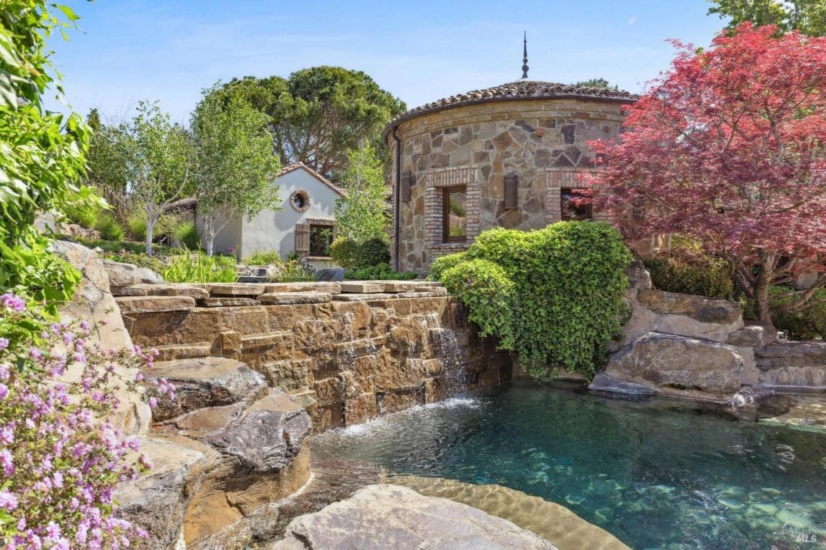 An outdoor scene featuring a pool and a stone structure surrounded by greenery.