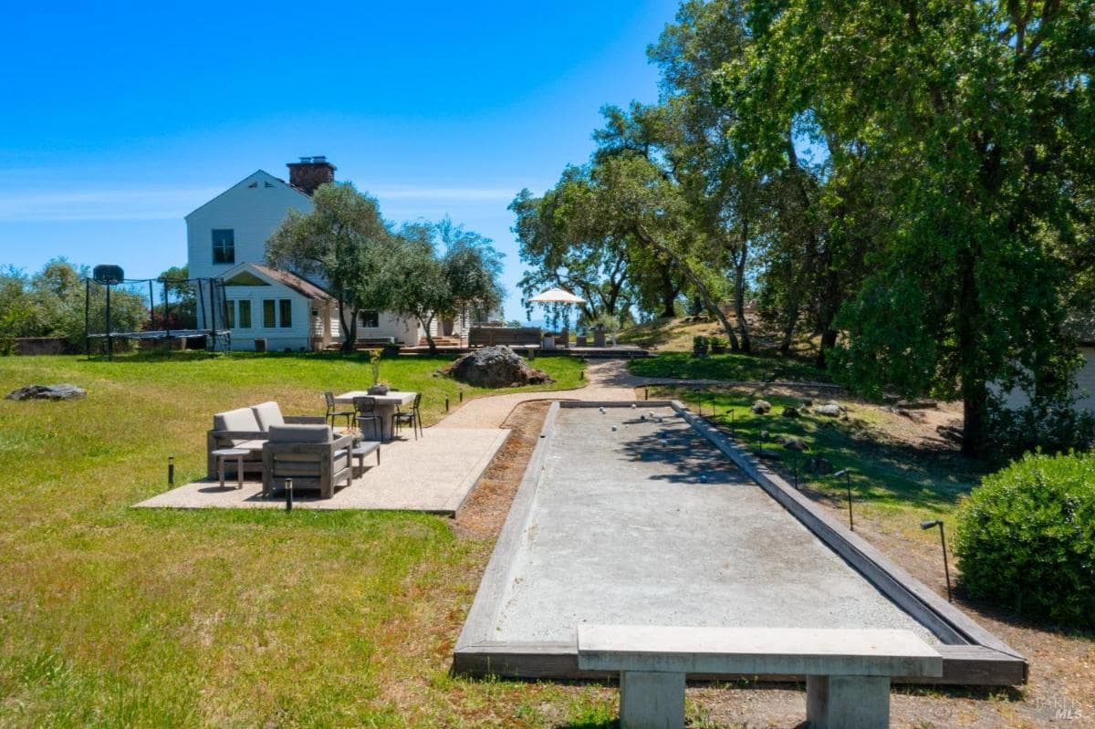 A bocce ball court is located in front of a house with seating nearby. 