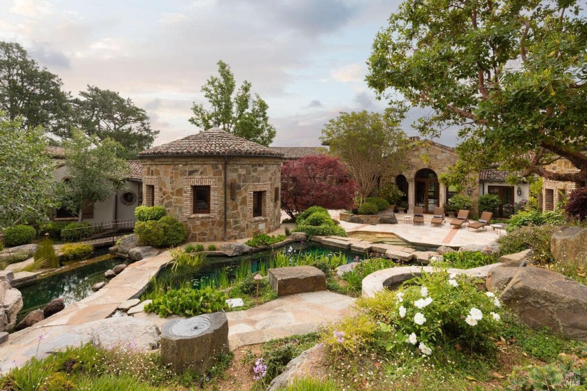 A landscaped outdoor area featuring a stone structure, a pool, and lush greenery.