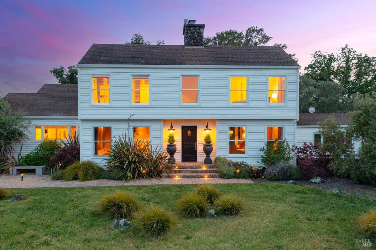 A two-story white house with illuminated windows and a stone pathway in front. 