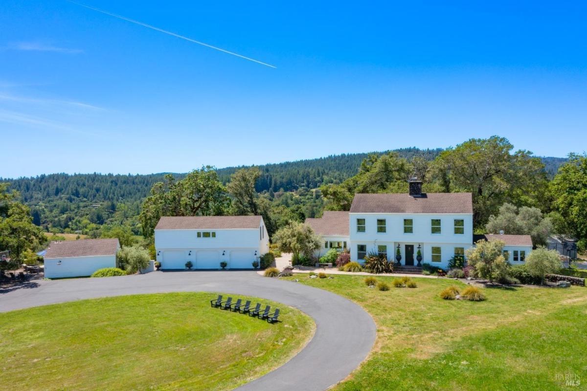 An aerial view of a white house with a garage and a circular driveway. 