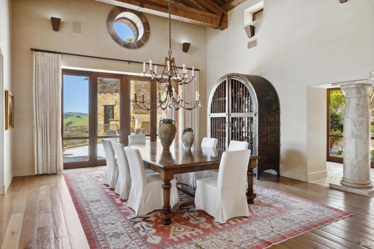 A dining room with a long wooden table, white chairs, and large windows.