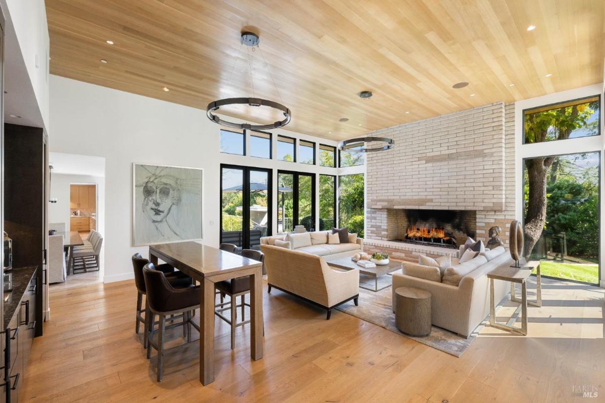 Open-plan living room with a dining table, sofas, a fireplace, and large windows with garden views.