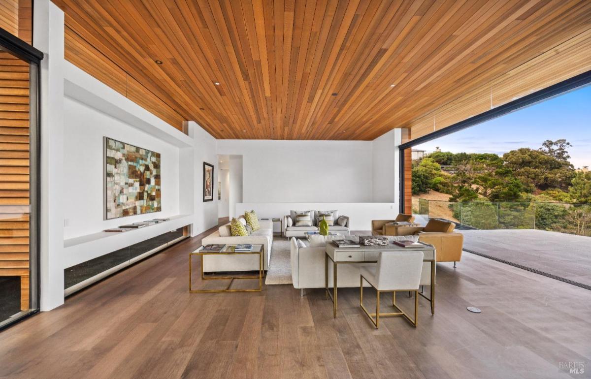 A living area with a wood-paneled ceiling, white walls, modern seating, and an open view.