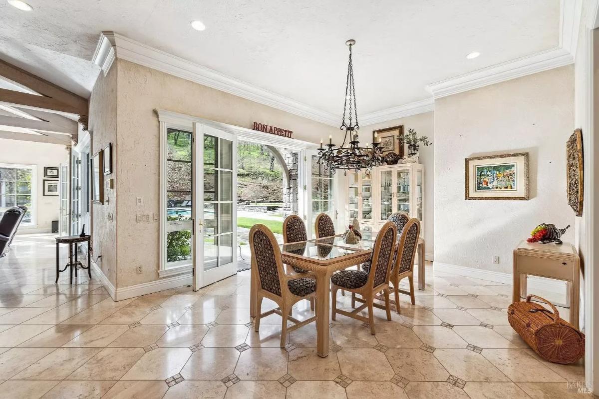 Dining area with tiled flooring with a rectangular dining table, chairs, and a chandelier near a wall of windows.