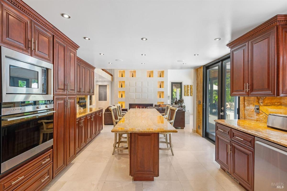 A kitchen featuring wooden cabinets, a large island with bar stools, and stainless steel appliances. 