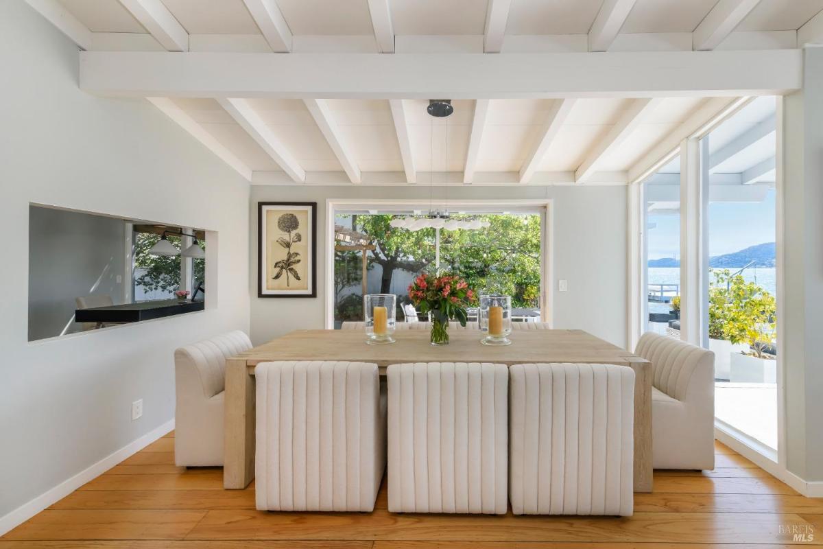 Dining room with padded chairs, wooden floor, and a view of an outdoor space through sliding glass doors.