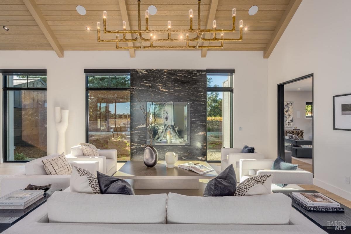 Living room with black stone fireplace, wood ceiling, chandelier, and seating area.