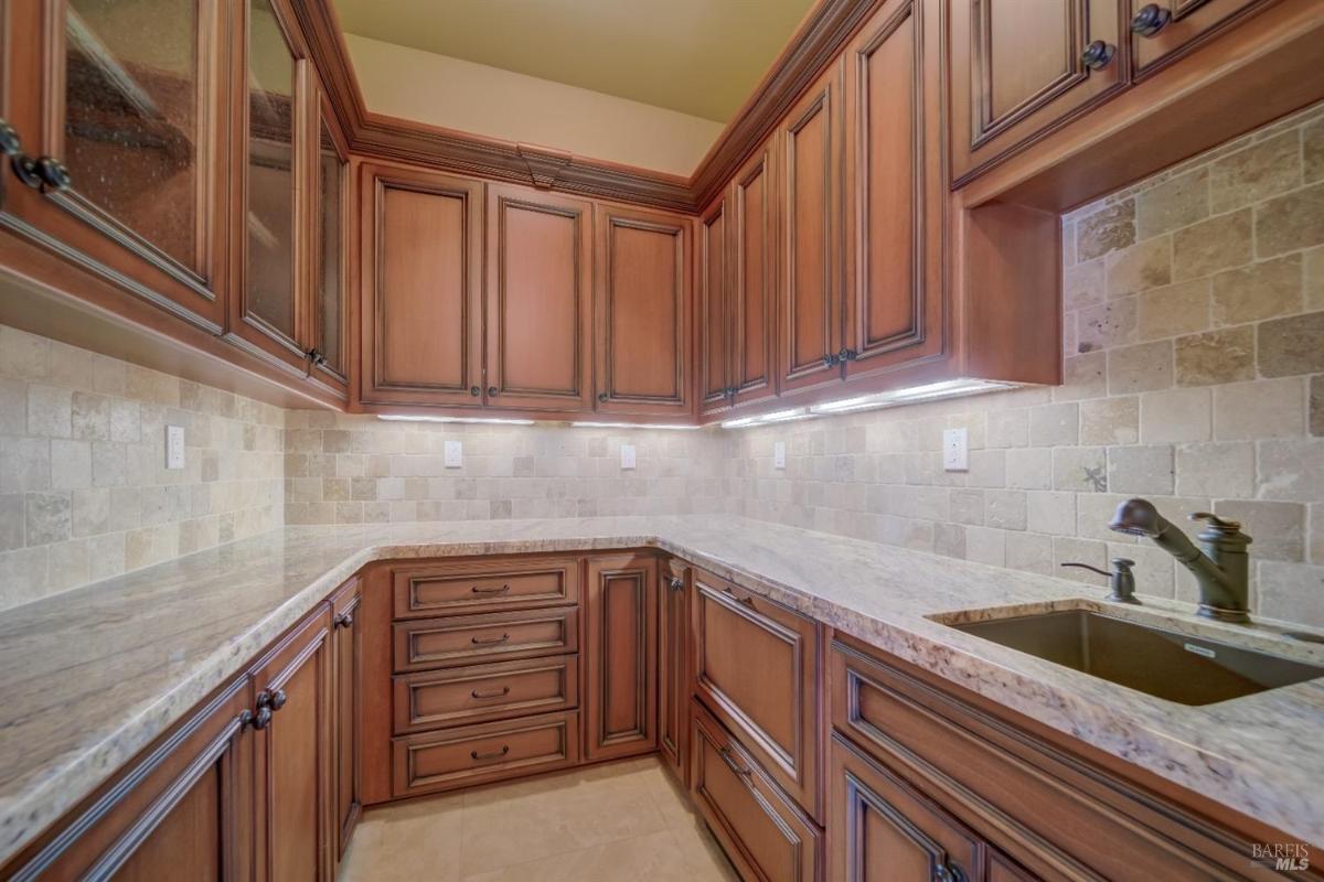 A corner kitchen with wooden cabinets, stone backsplash, and a small sink.