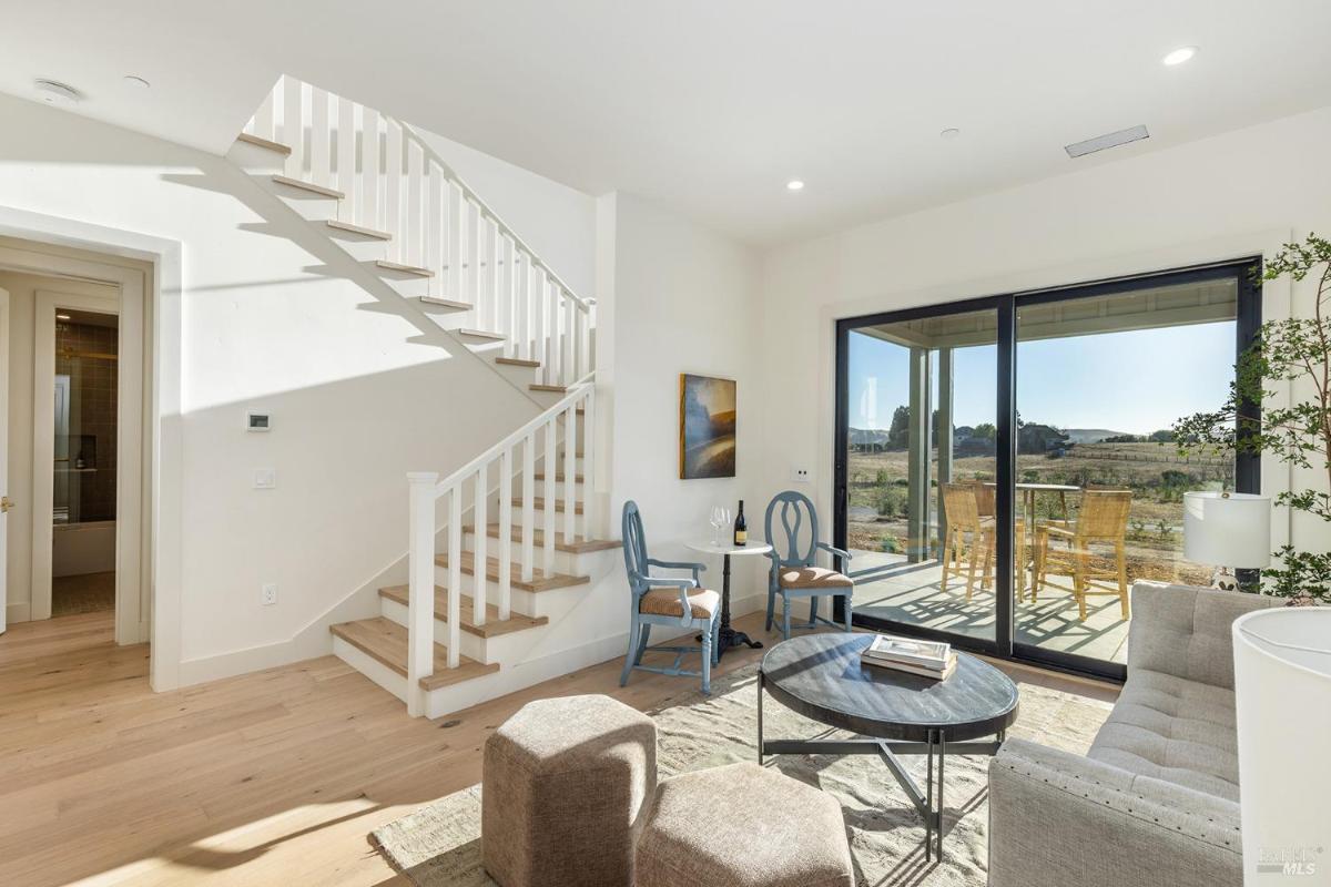 A living area with a staircase, chairs, and a sliding door leading to an outdoor view.