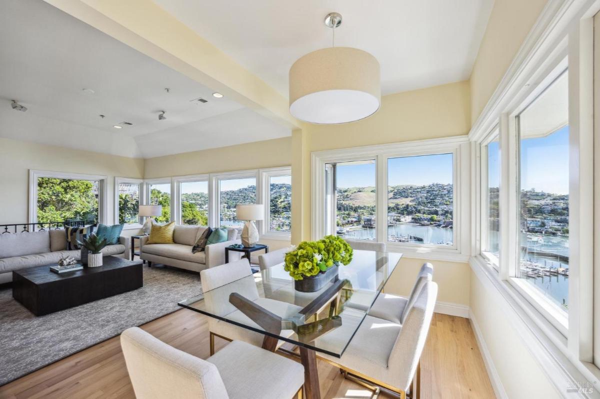 Dining area with a glass table and surrounding windows overlooking water and hills