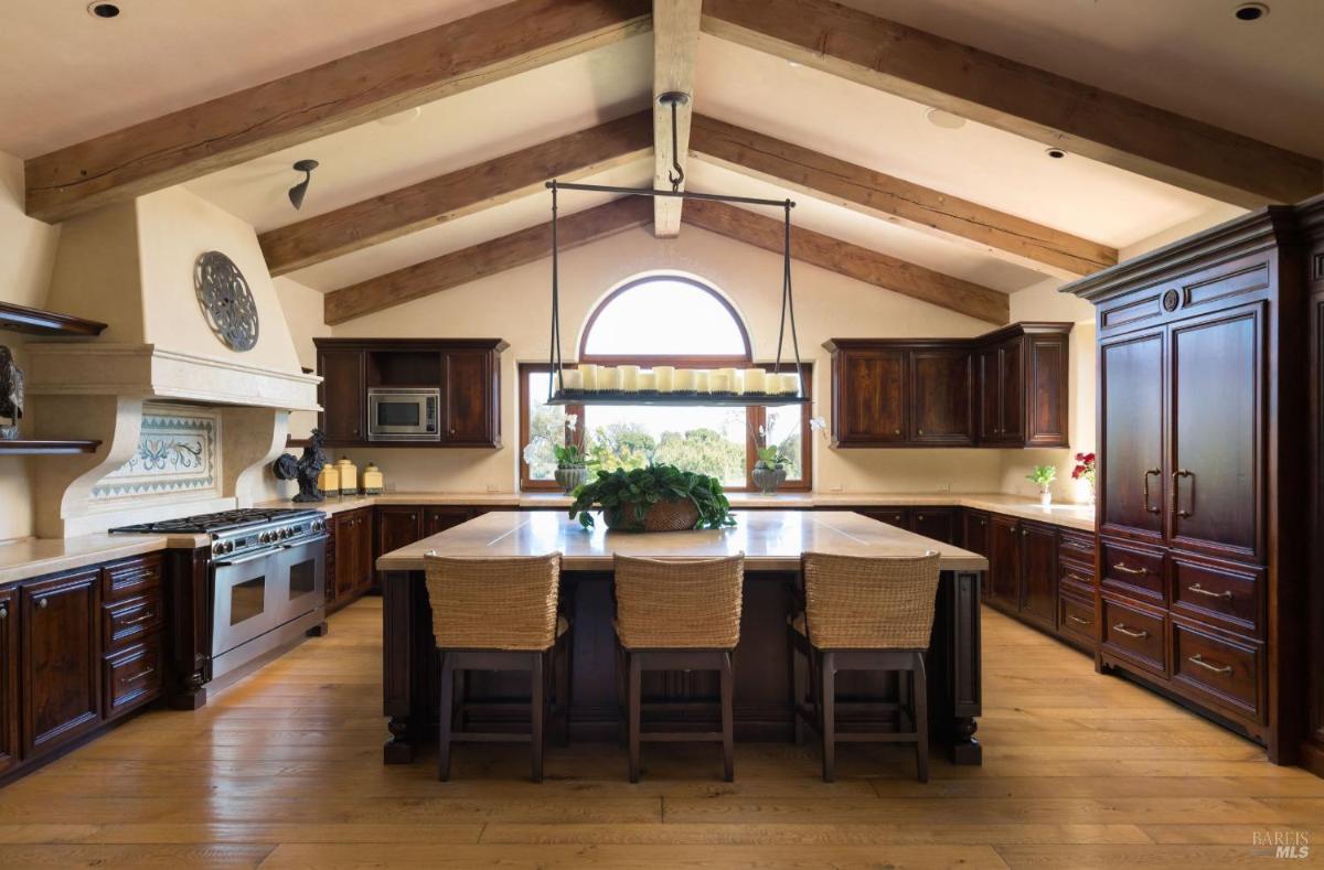 A kitchen with wood cabinetry, a large island, and exposed beams.