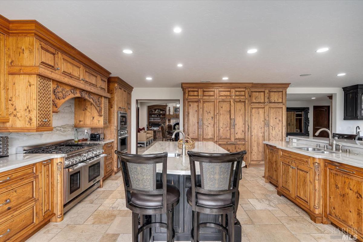 Kitchen with wood cabinetry, marble countertops, and a central island with chairs.