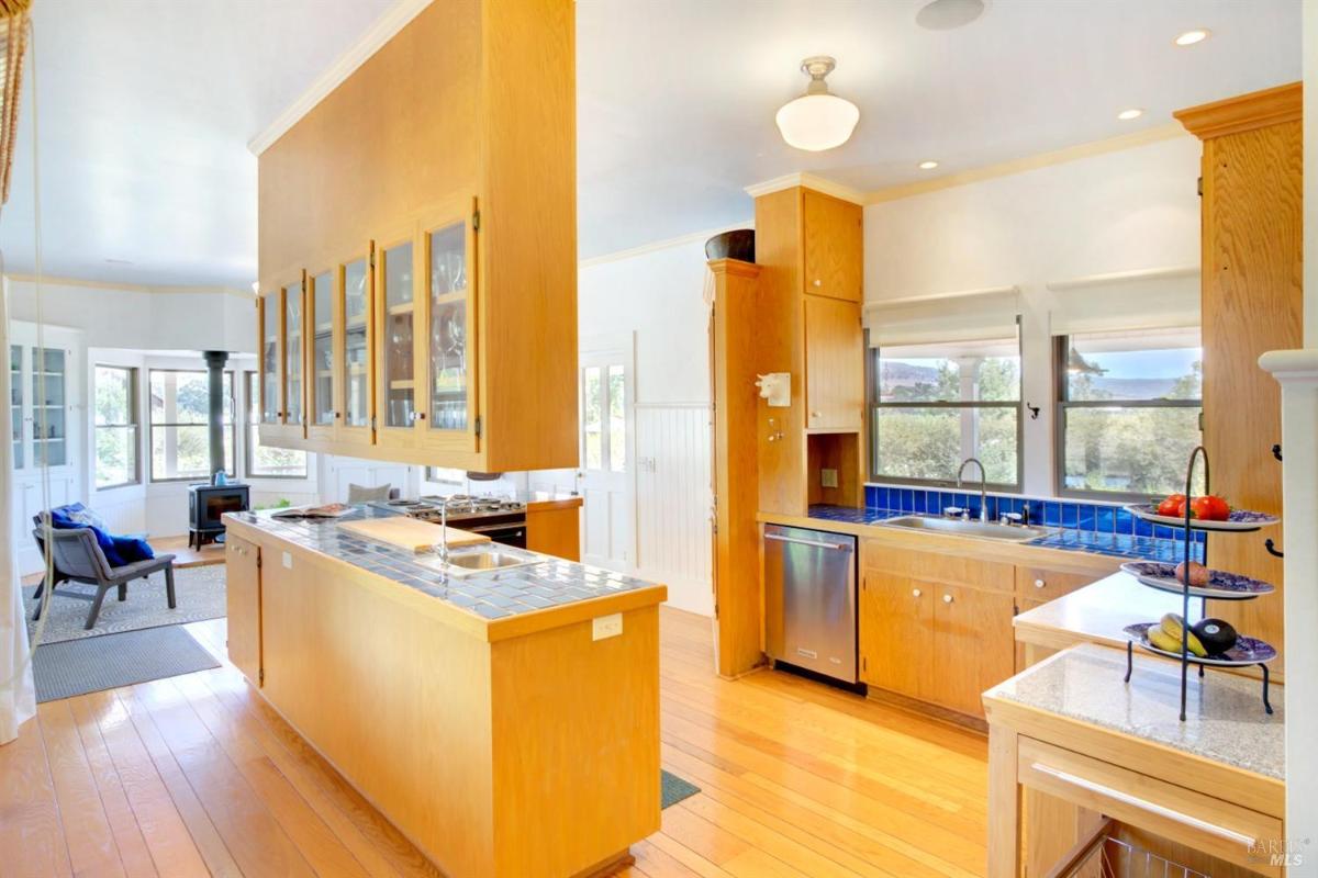 A kitchen with wooden cabinets, blue tile counters, and stainless steel appliances, opening to a seating area.