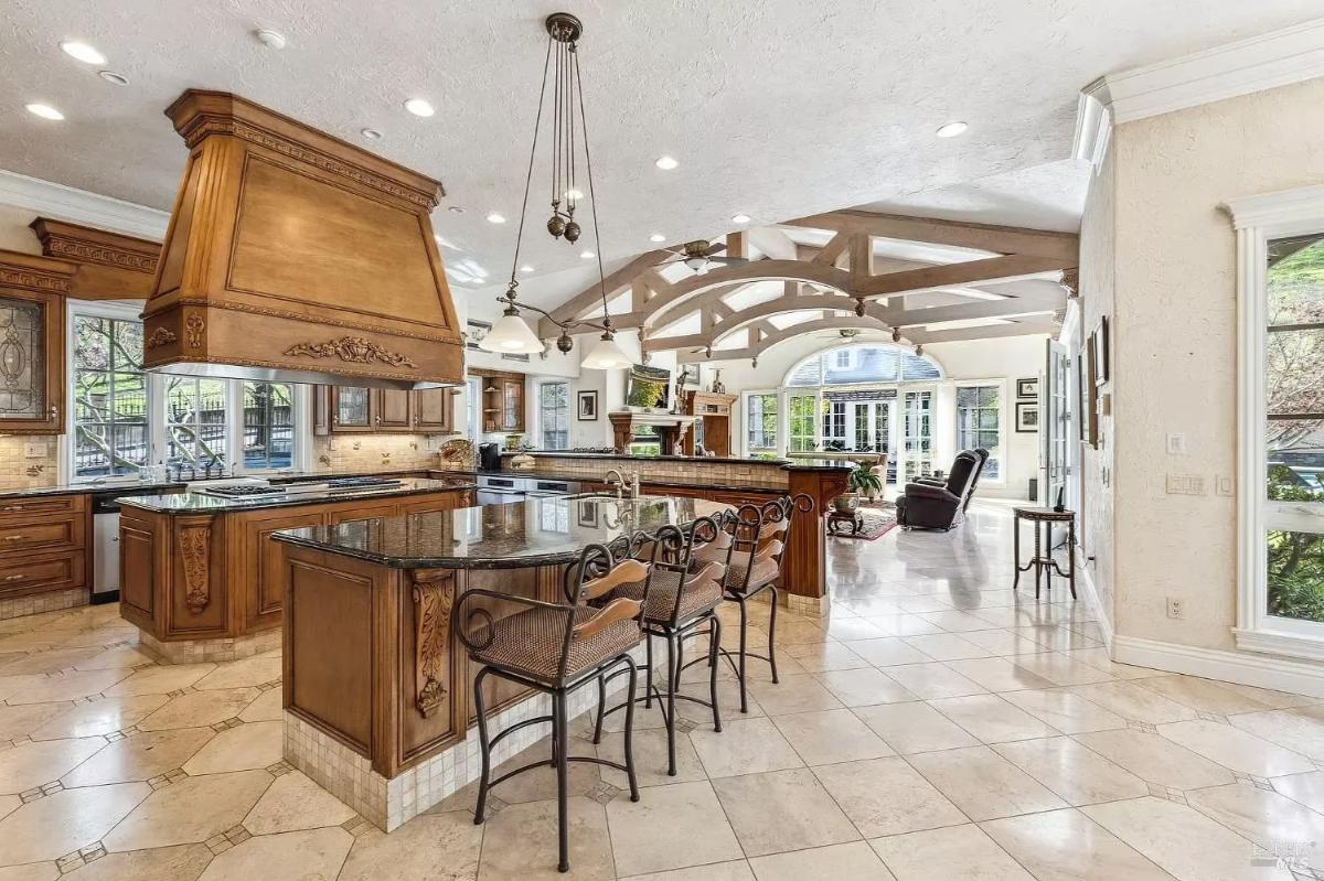 A kitchen with granite countertops, a large wooden hood, and an island with bar seating.