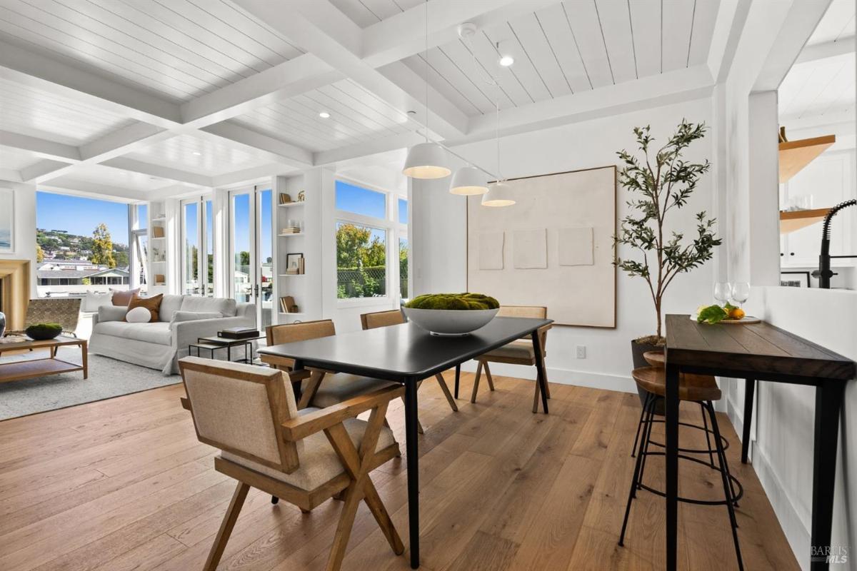 A dining area with a black table, light wood chairs, and a pendant light fixture.