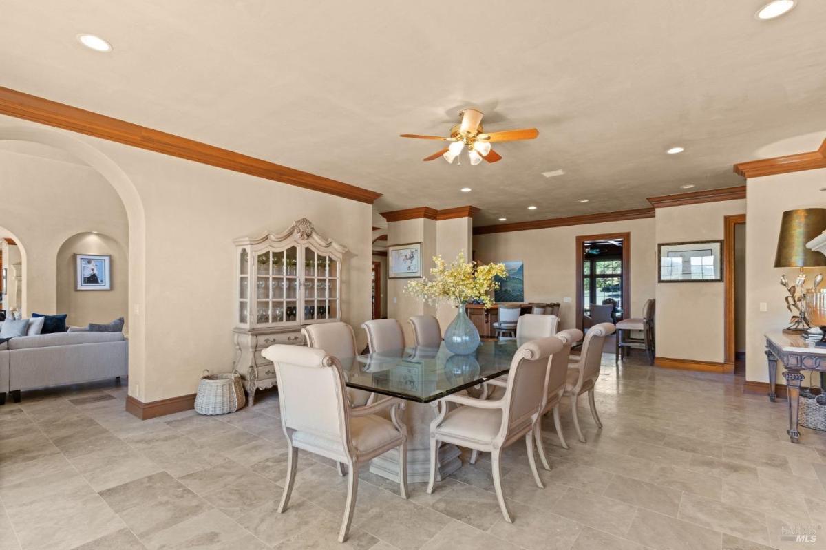 A formal dining room with an ornate hutch, ceiling fan, and seating for eight beneath elegant crown molding.