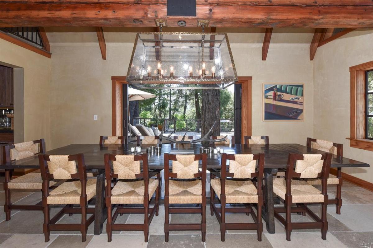 A dining room with a long table, woven chairs, and a chandelier.