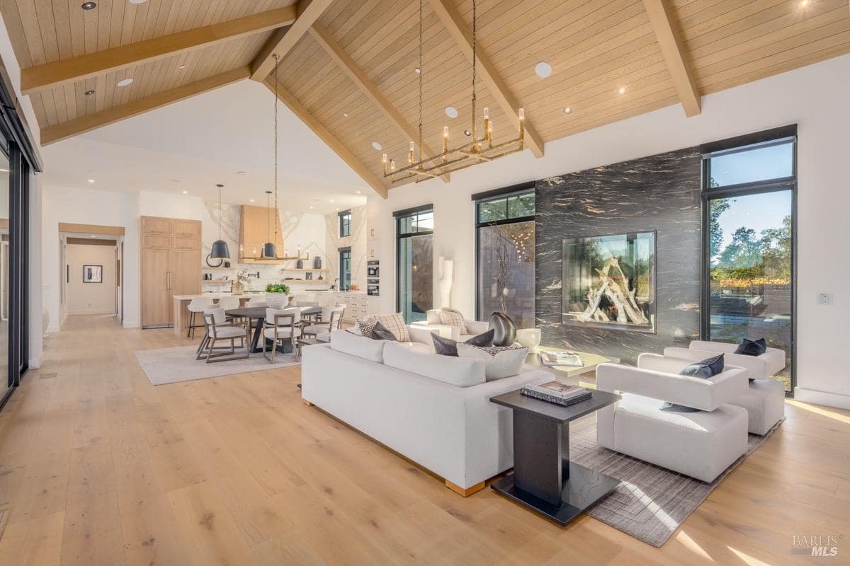 Open living area with black stone fireplace, wood ceilings, seating, and adjacent dining and kitchen spaces.