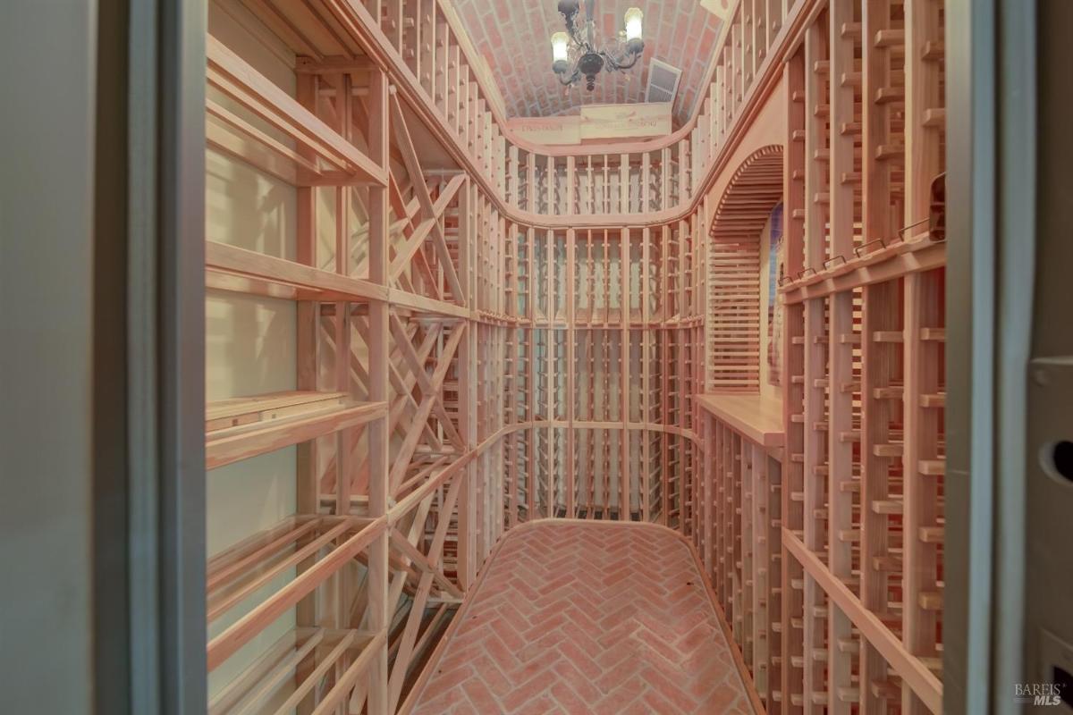 A wine cellar featuring wooden racks, a brick floor, and a vaulted ceiling with a chandelier.