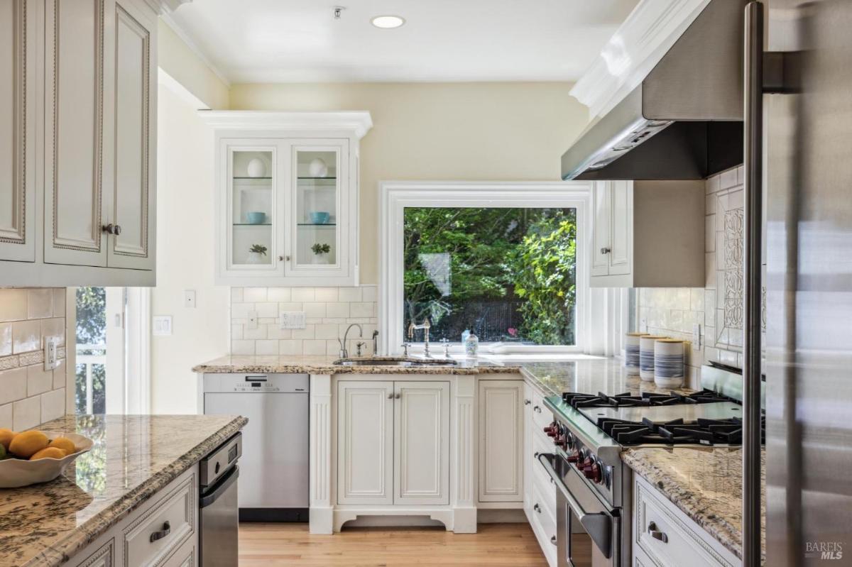 Kitchen with light cabinetry, granite countertops, and a window view of greenery.