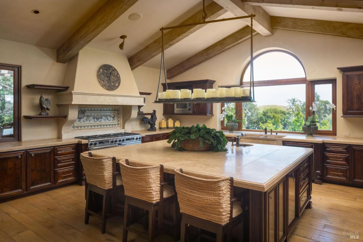 A kitchen with wood cabinetry, a large island, and exposed beams.