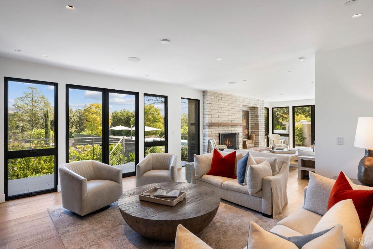 A lounge area with large windows, a round wooden coffee table, two chairs, and a sofa with cushions.