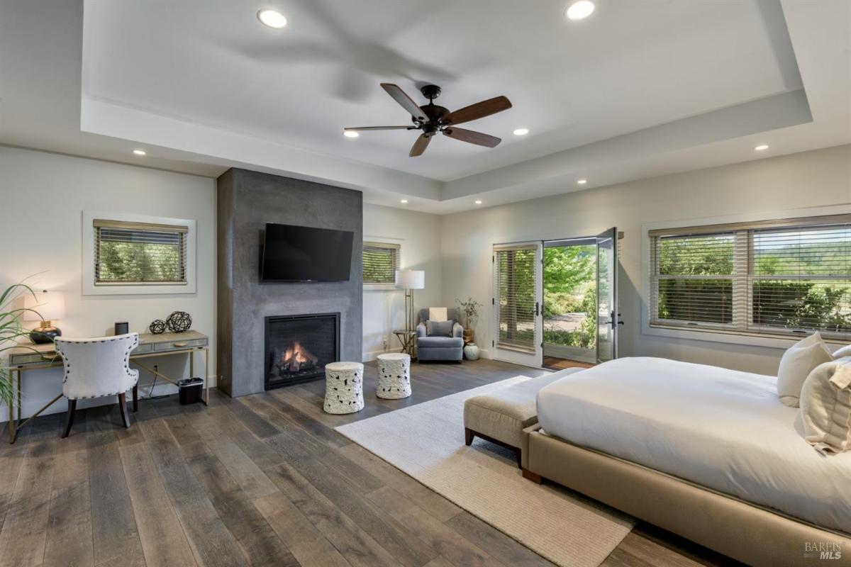 Bedroom with a fireplace, ceiling fan, desk, and patio doors.