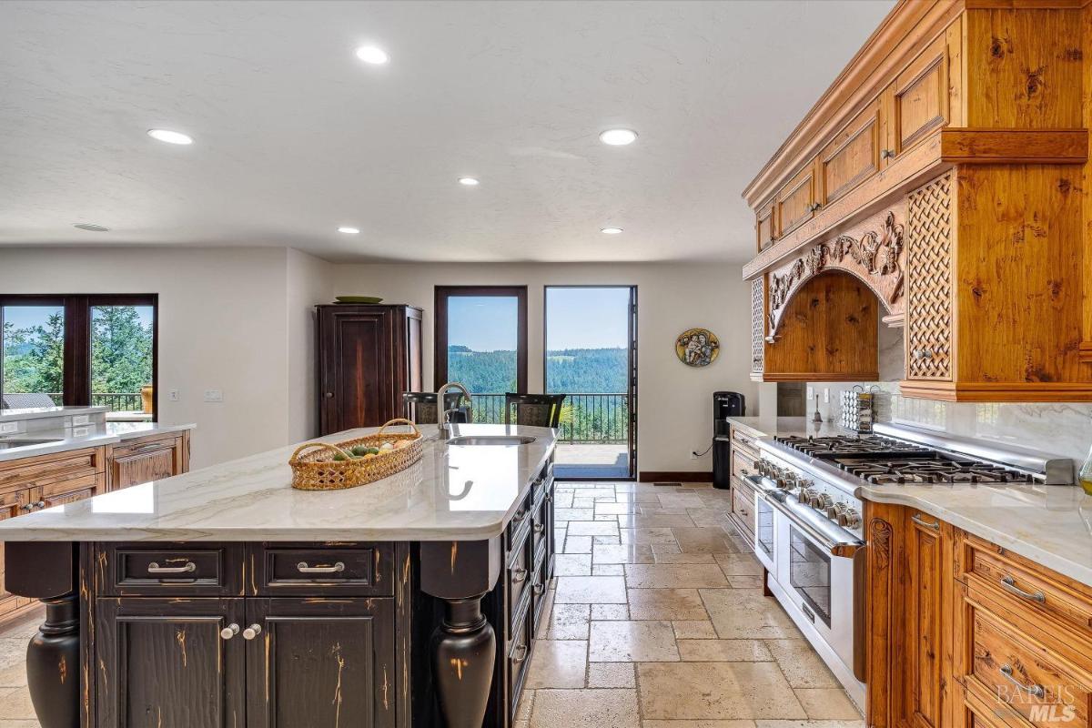 Kitchen with wood cabinetry, marble countertops, and a central island with chairs.