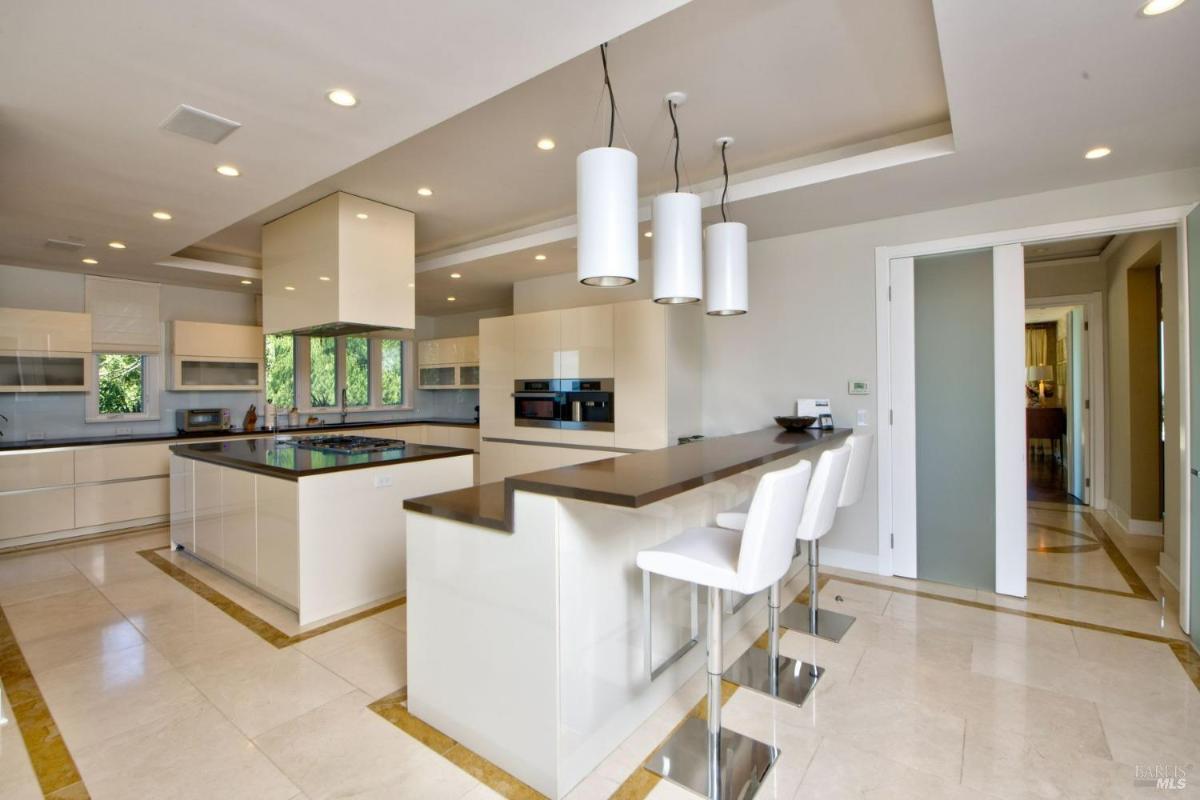 Modern kitchen with high-gloss cabinetry, a central island, pendant lighting, and an integrated breakfast bar with bar stools.