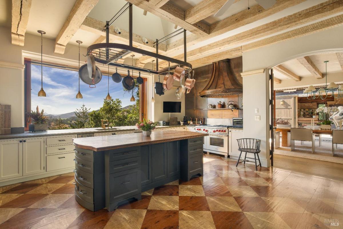 Kitchen with an island, hanging pots, a large window, and wooden ceiling beams.