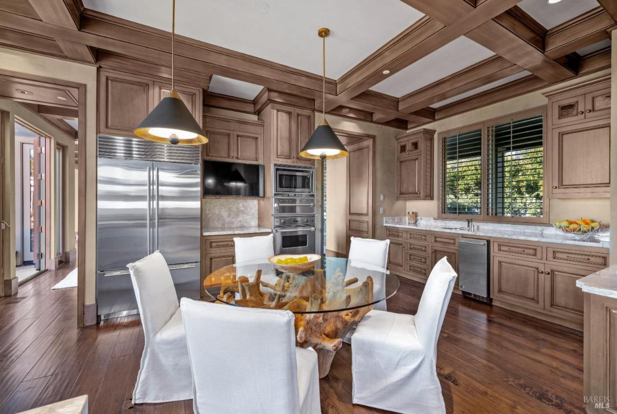 A kitchen featuring a glass table with six white chairs, wooden cabinets, and stainless steel appliances.