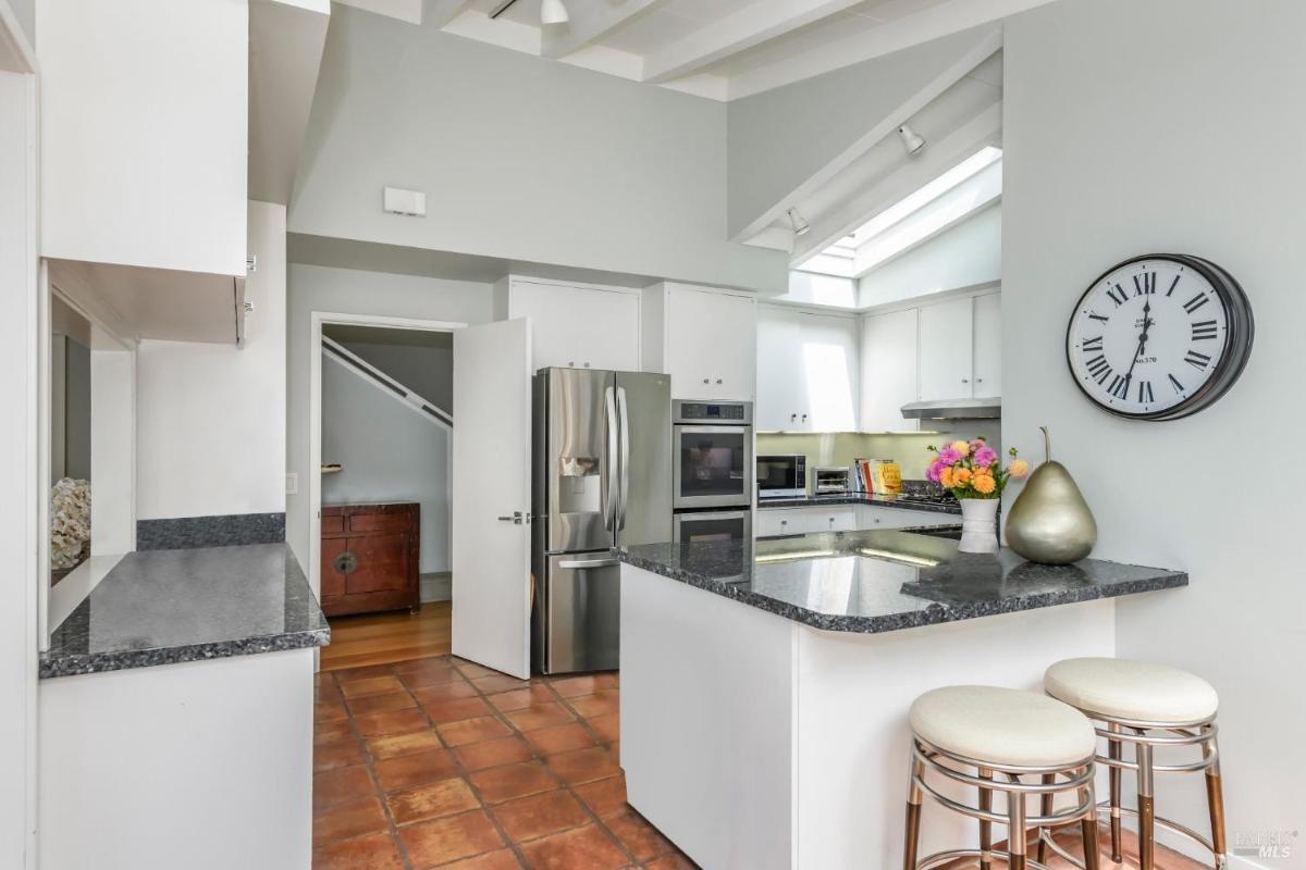 A kitchen with granite countertops, stainless steel appliances, and terracotta floor tiles.