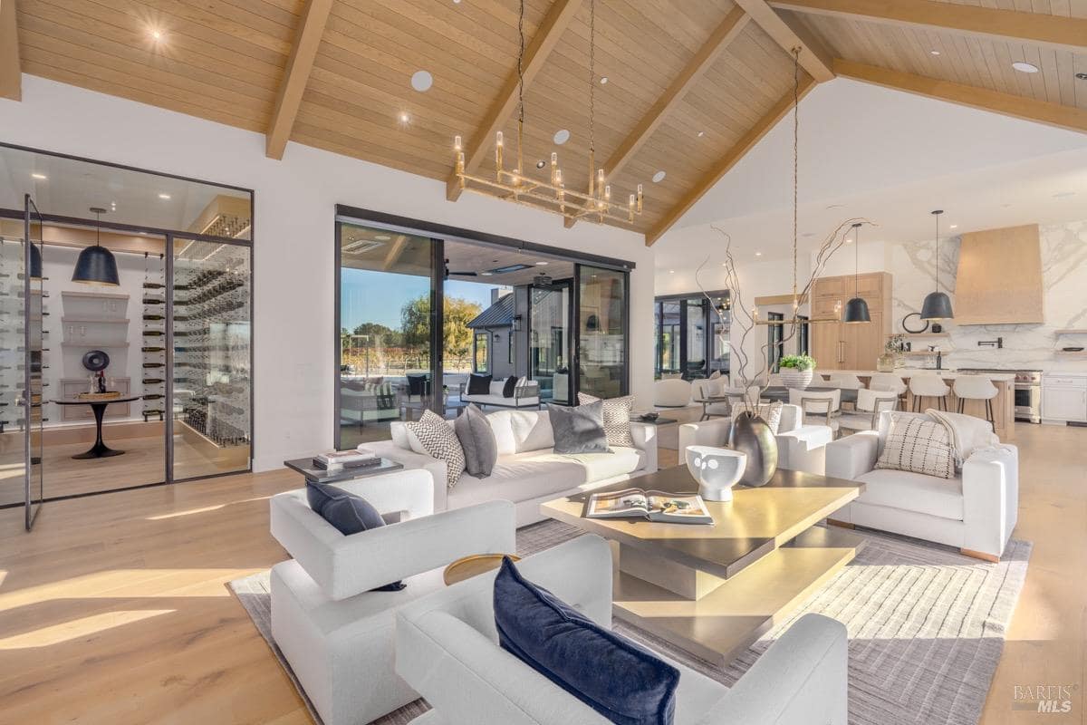 Open living area with black stone fireplace, wood ceilings, seating, and adjacent dining and kitchen spaces.