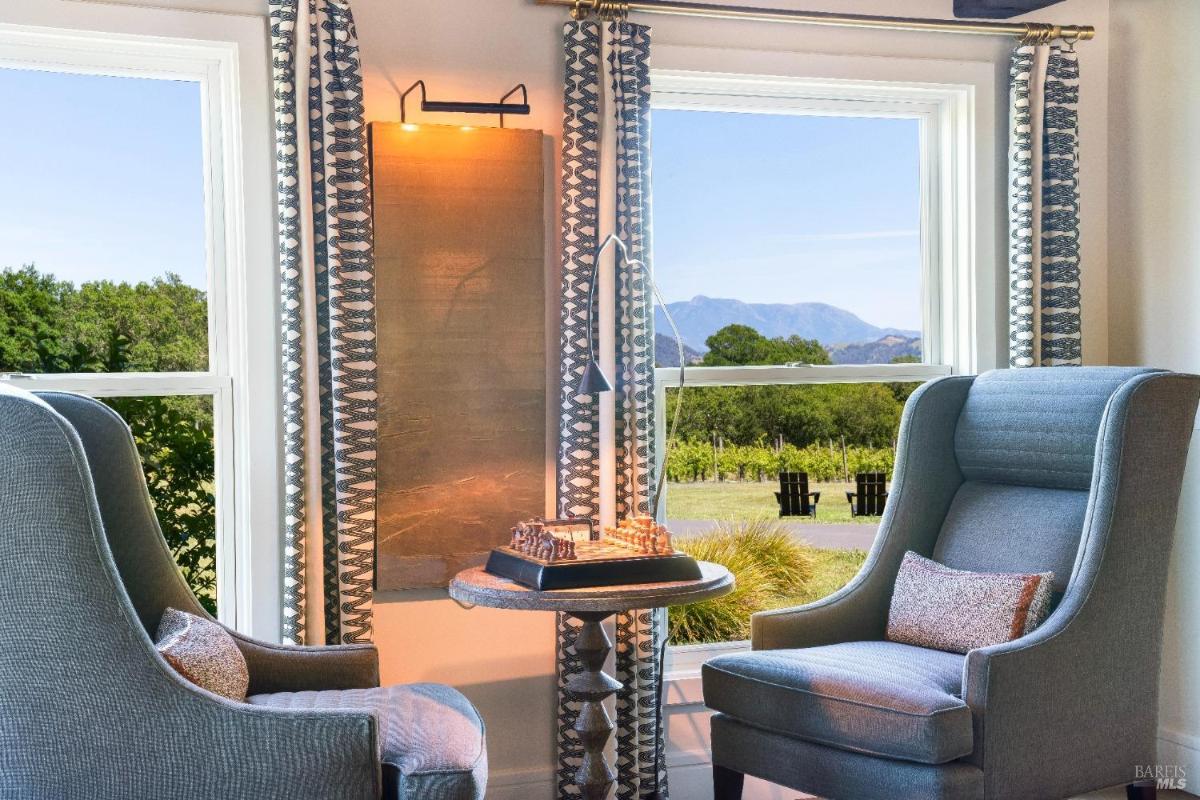 Close-up of chairs and a chess table with views of vineyards through windows.