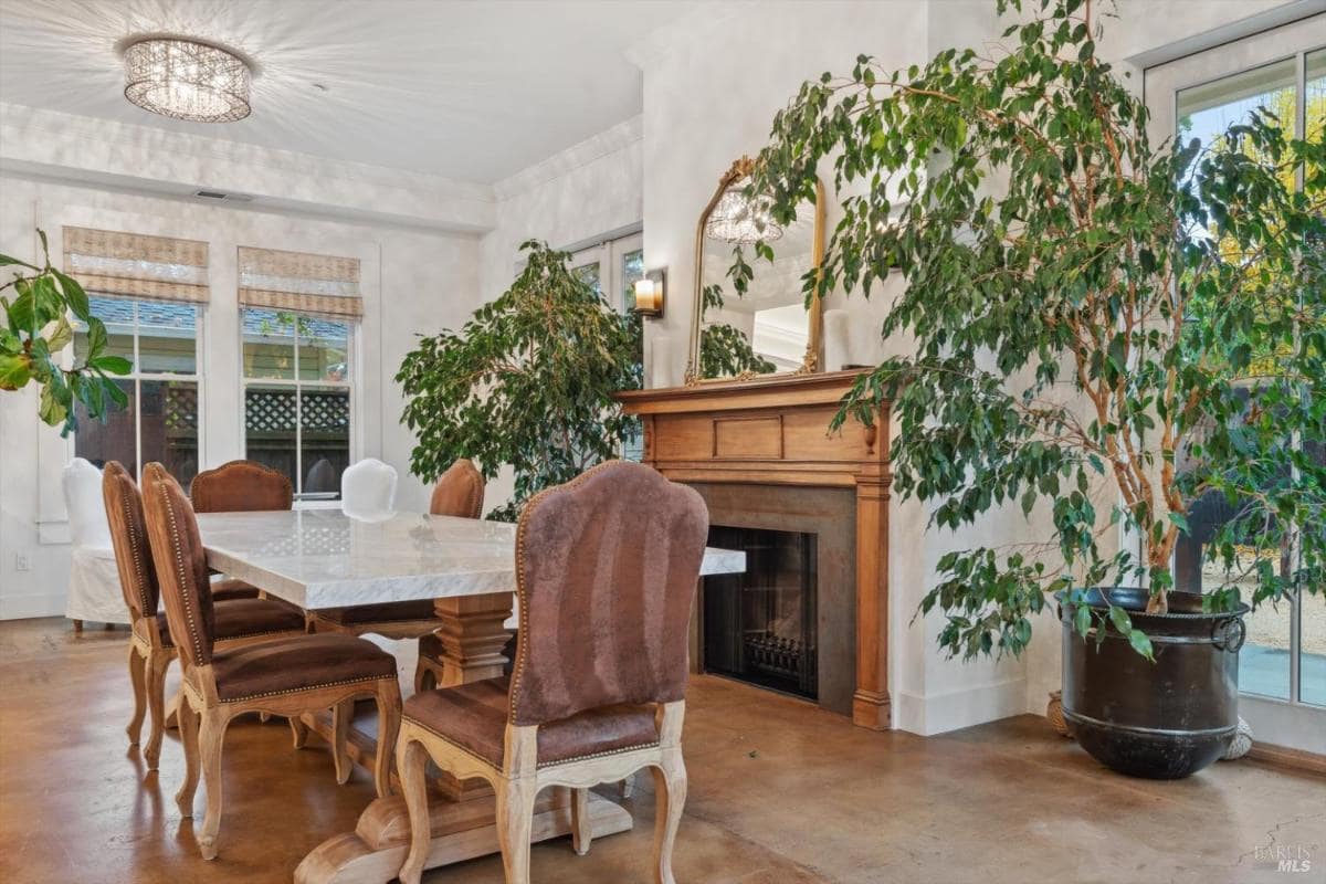 Dining area with a marble table and wooden chairs, adjacent to large windows.