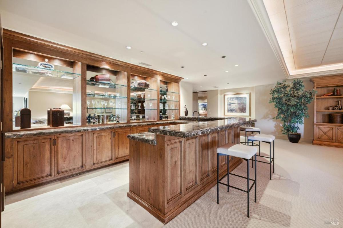 A bar area with glass shelving, wood cabinets, and a marble countertop.