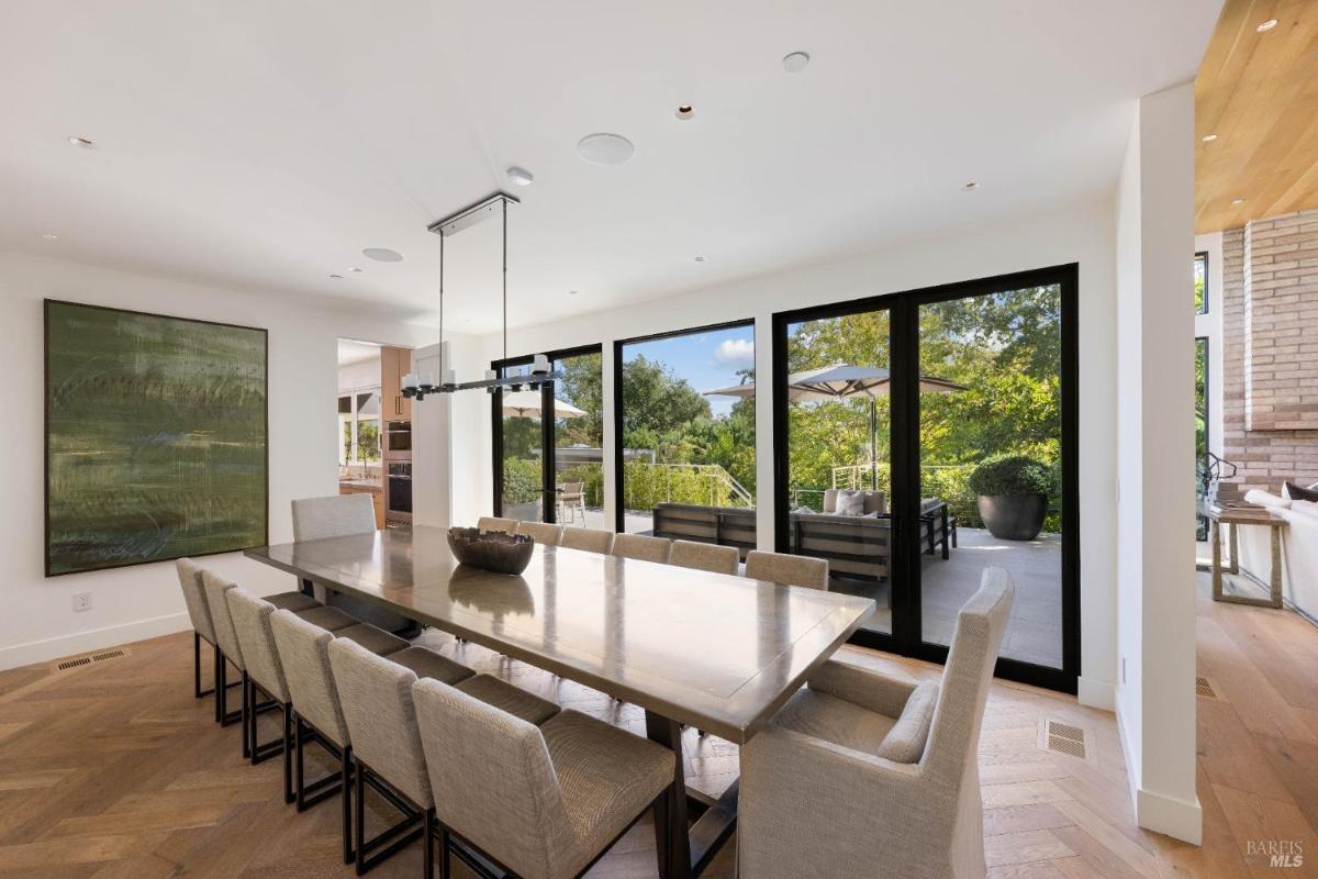 A dining room with a rectangular dining table, upholstered chairs, a light fixture, and glass doors leading outside.